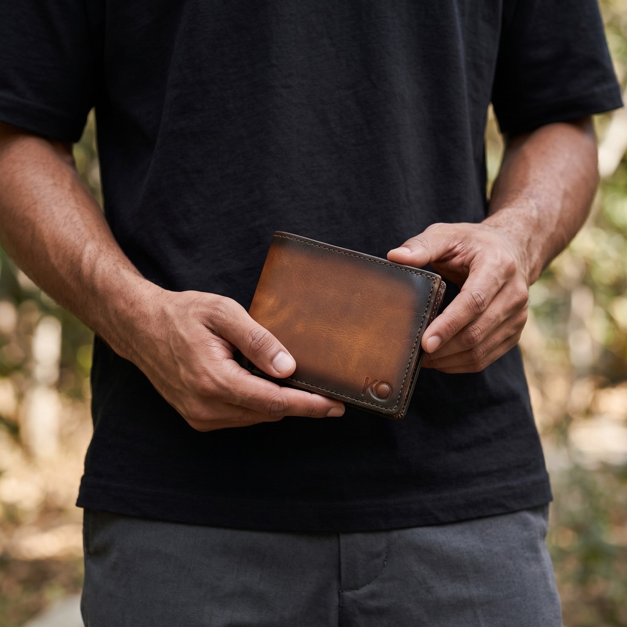 Billetera kopelletteria de cuero vacuno con acabado difuminado de coñac a café y protección RFID en manos de un hombre