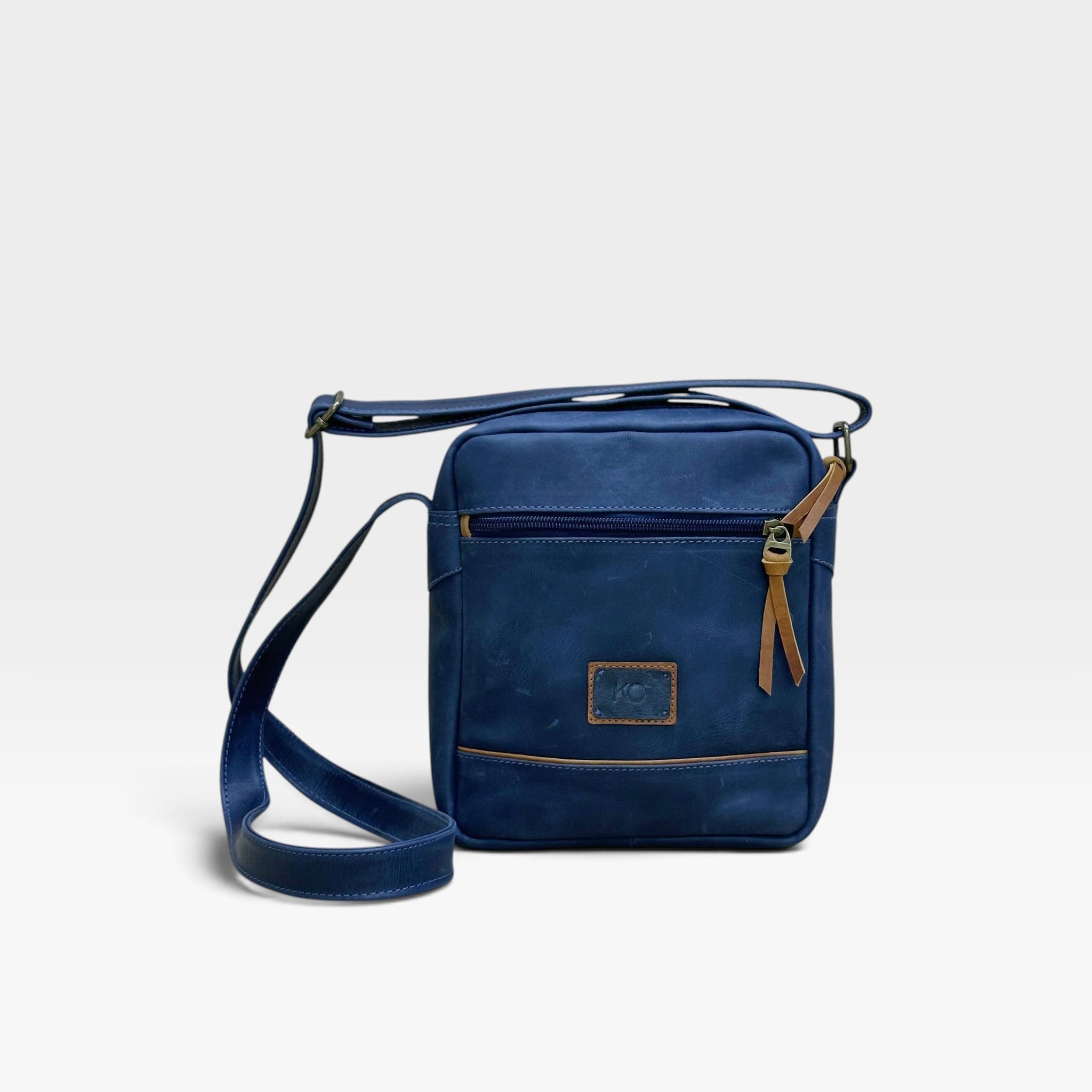 Bolso manos libres kopelletteria en cuero rústico azul profundo con detalles en color miel y correa ajustable.