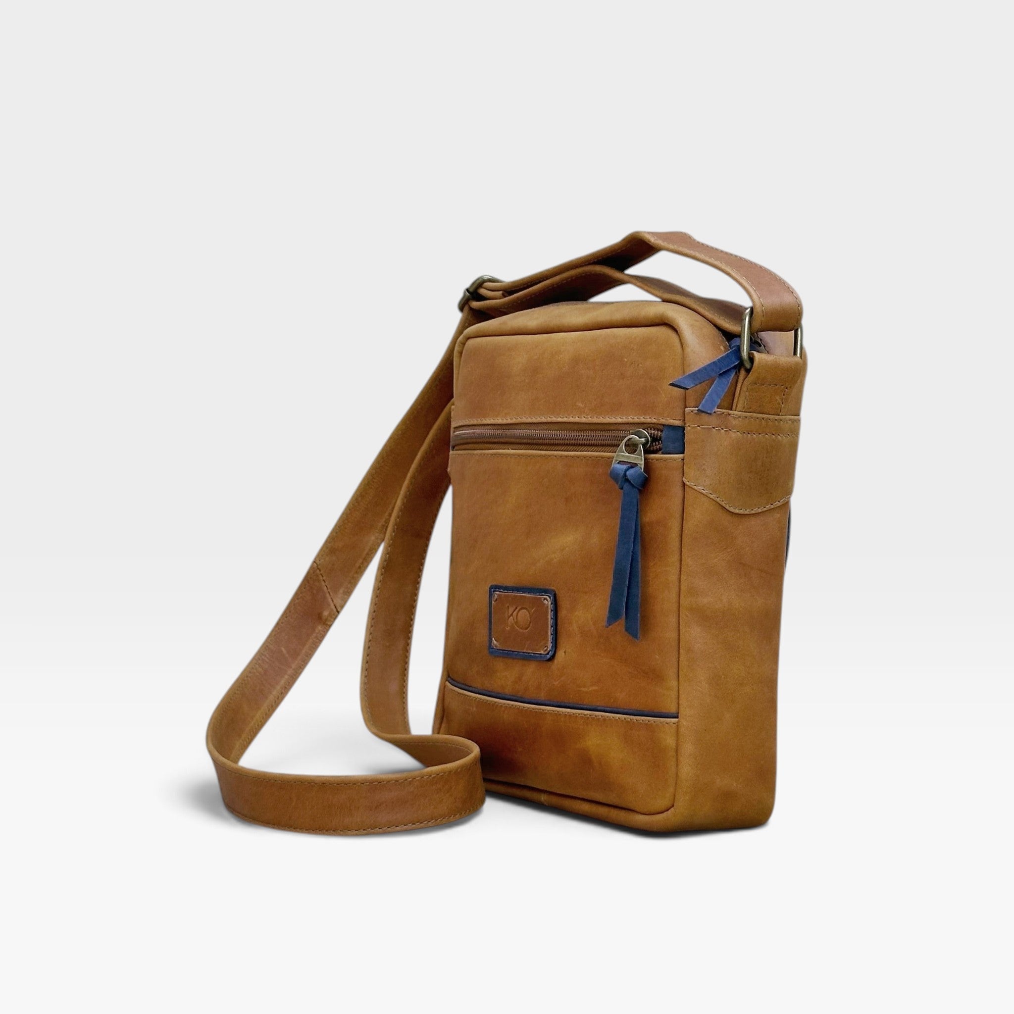 Bolso manos libres kopelletteria de cuero rústico marrón ocre con detalles en azul y correa ajustable para hombre.