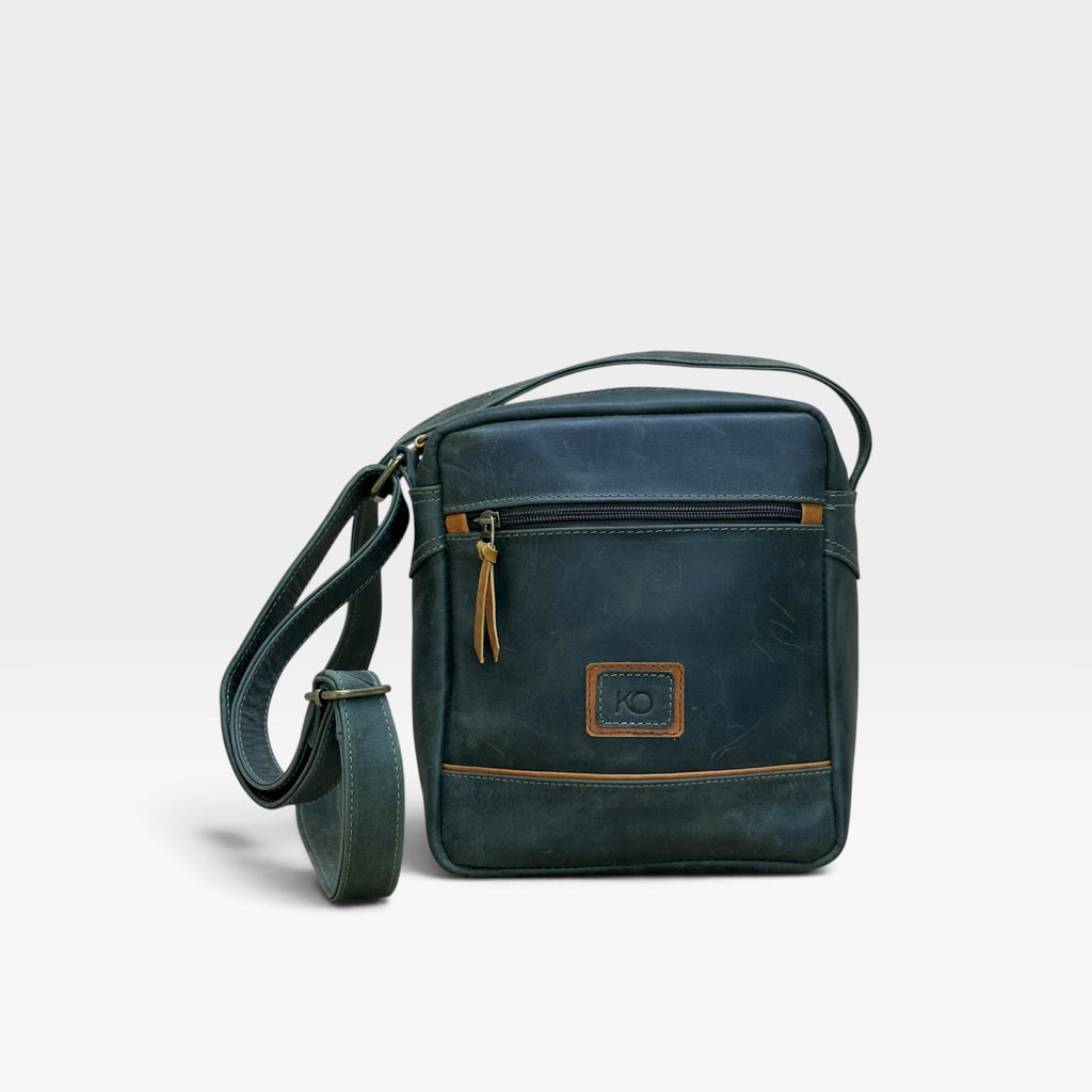 Bolso manos libres kopelletteria en cuero rústico azul profundo con detalles en color miel y correa ajustable.