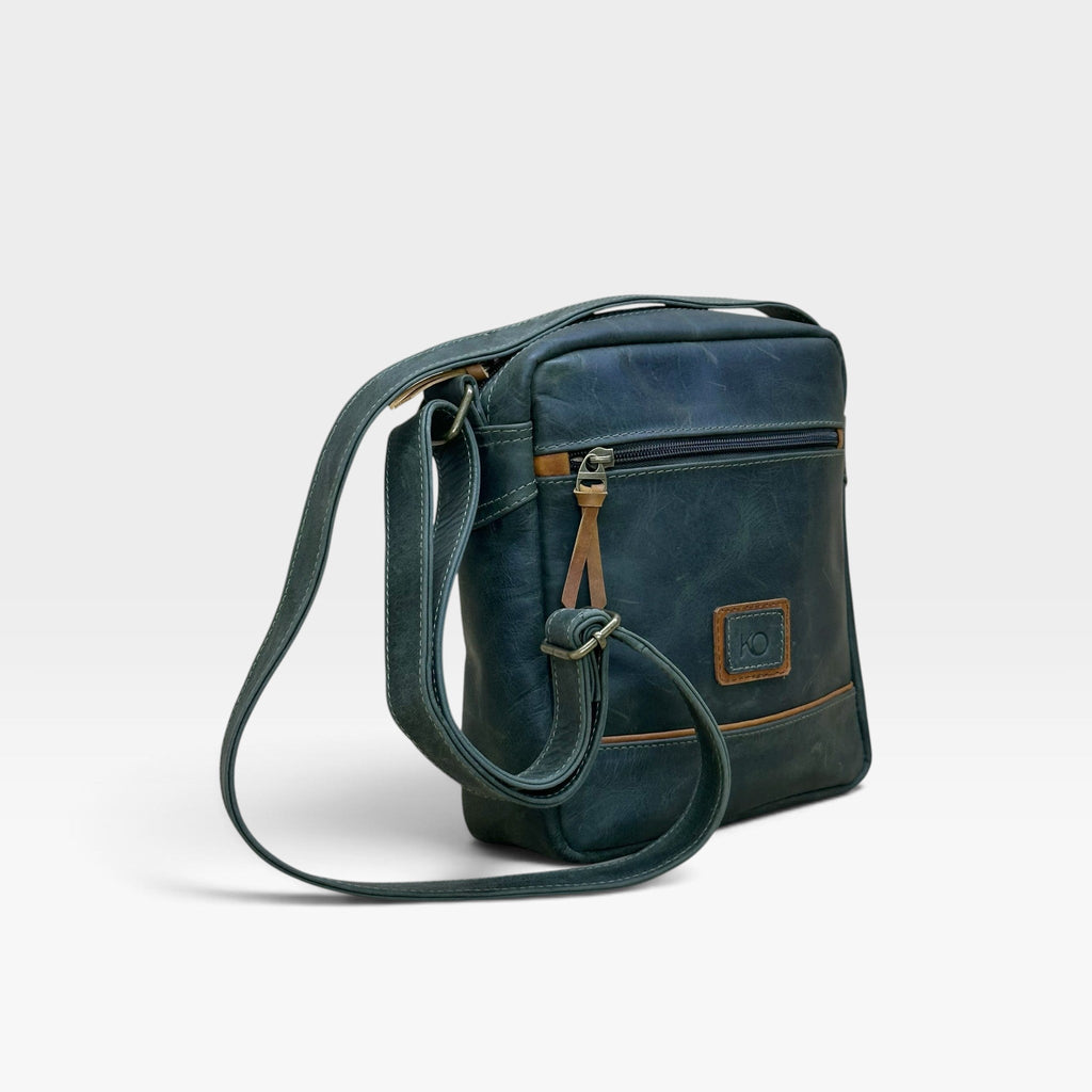 Bolso manos libres kopelletteria en cuero azul profundo con detalles en color miel y correa ajustable.