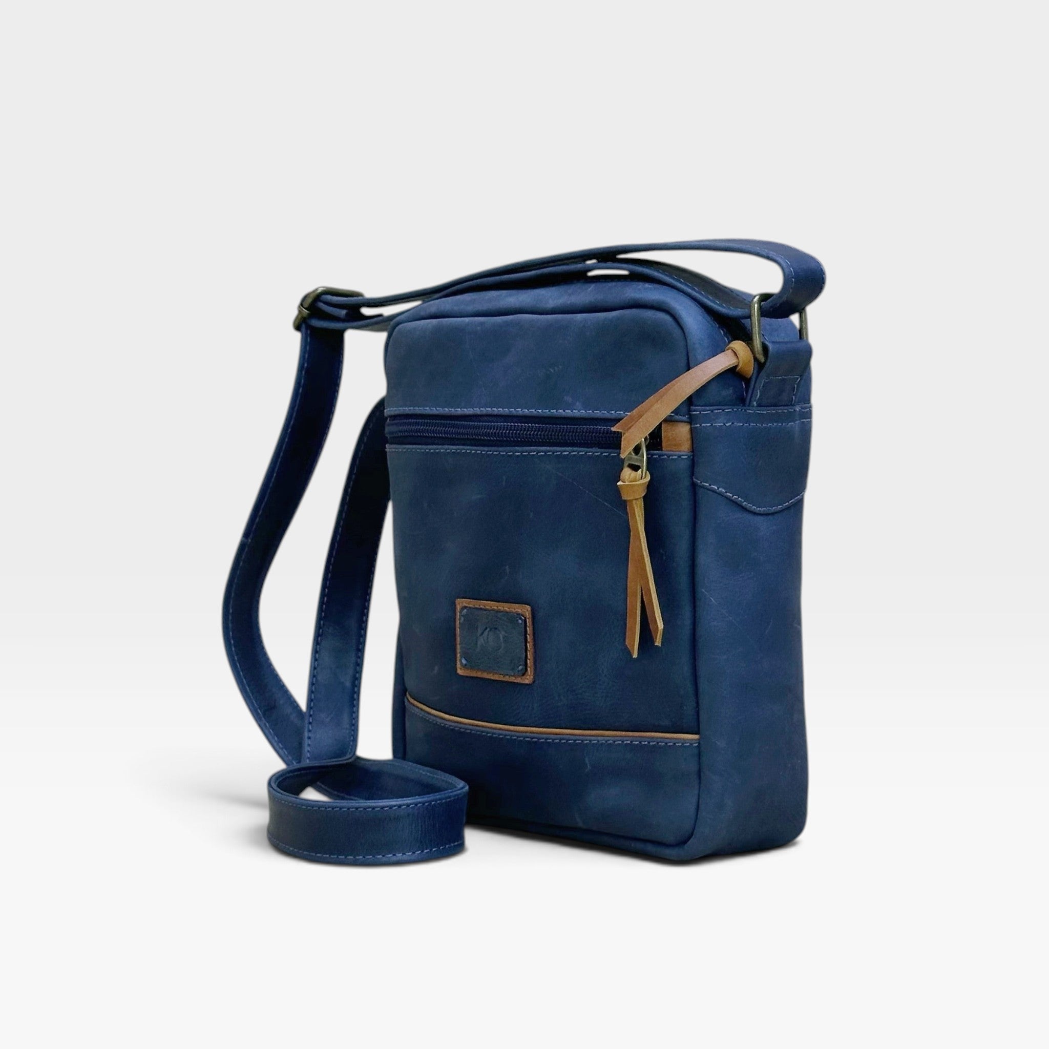 Bolso manos libres kopelletteria en cuero azul profundo con detalles en color miel y correa ajustable para hombre.