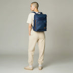 Persona con morral kopelletteria azul de cuero genuino, diseño minimalista con compartimento para laptop y detalles.
