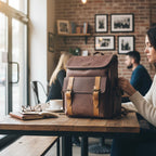 Morral urbano kopelletteria de cuero marrón con detalles microperforados y correas en tono ocre sobre mesa de café.